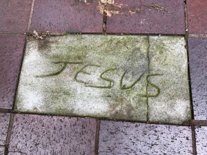 Jesus written in concrete on a sidewalk in the city